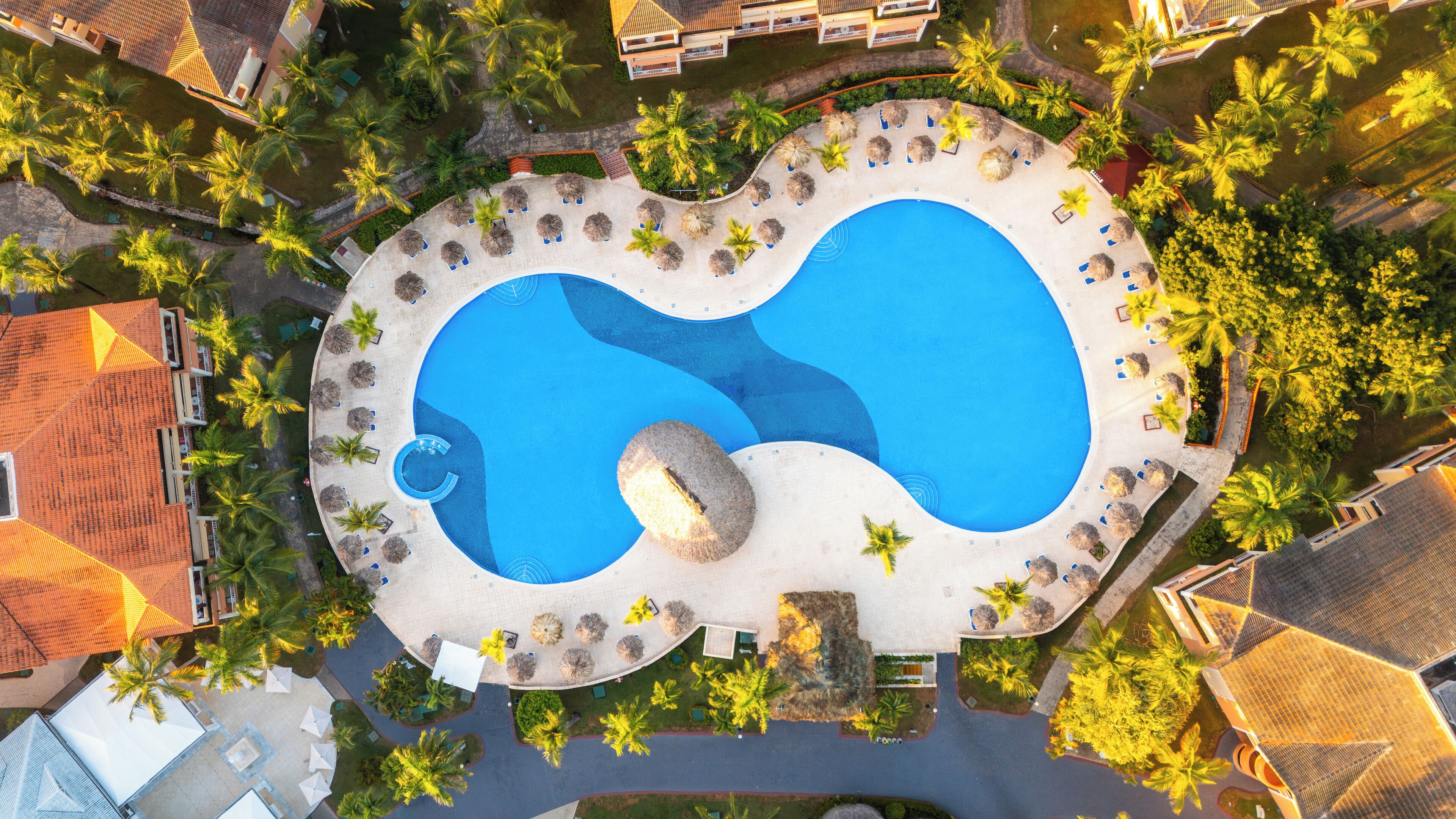 An aerial view of a resort with a large pool, palm trees, and resort buildings.