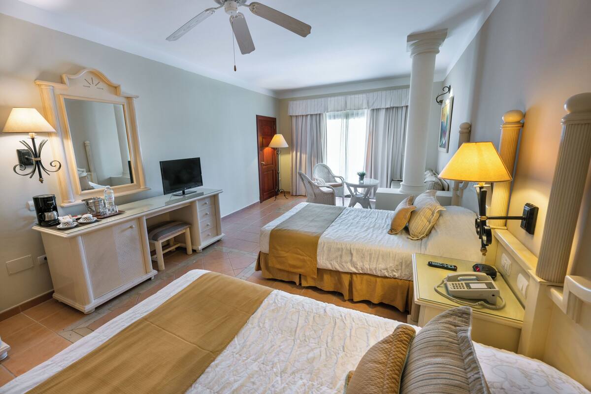 Habitació d'hotel amb dos llits, una escriptori amb un ordinador, una televisió, una cadira, una làmpada i un telèfon.