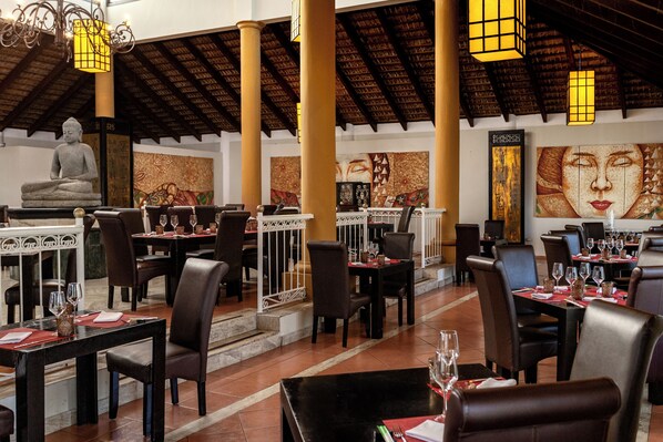A restaurant with tables set for dining, a Buddha statue, and decorative wall art. - Bahia Principe Explore Turquesa - Hyatt Inclusive Collection - All Inclusive (Punta Cana)