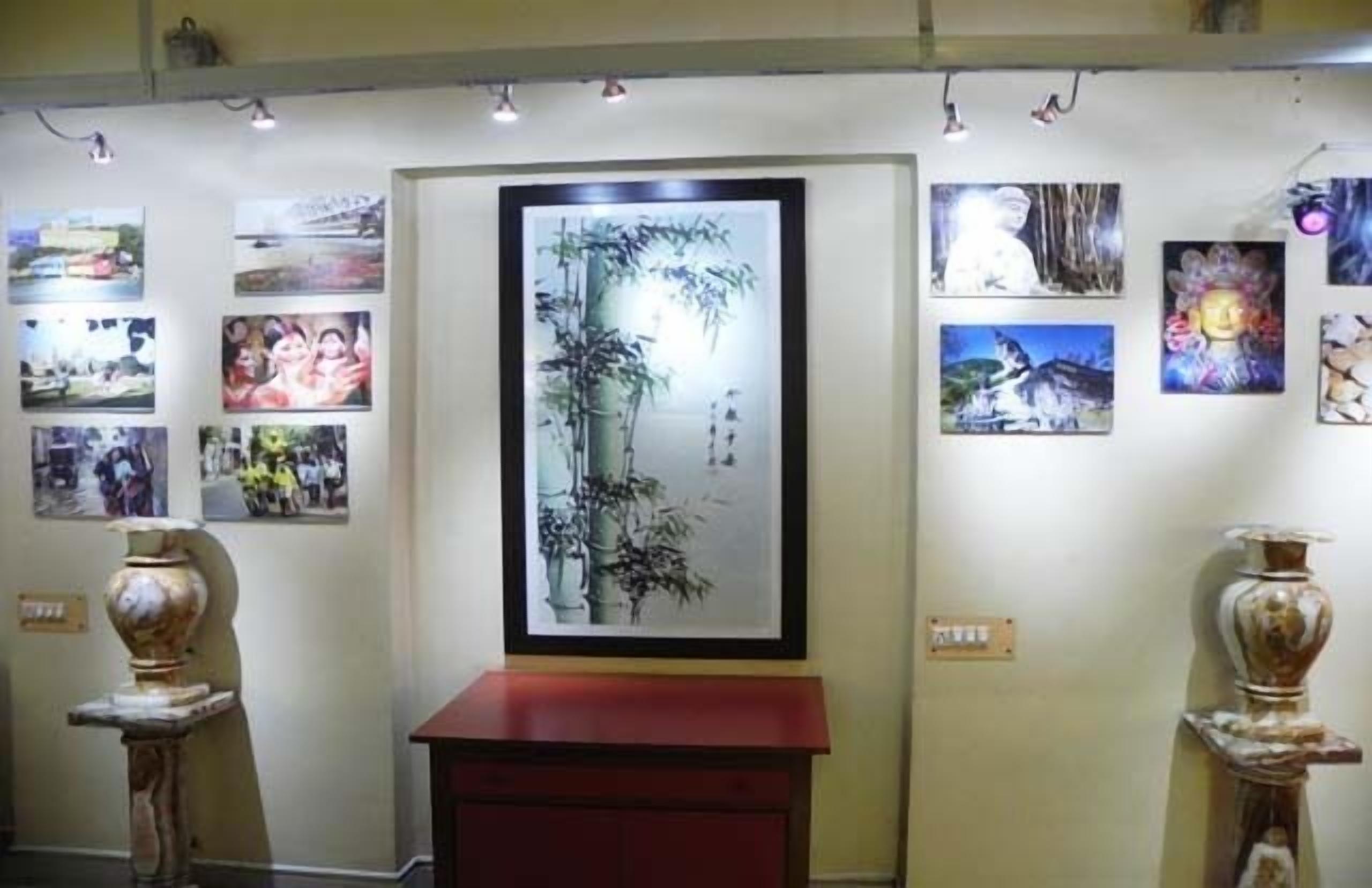 A gallery with framed artworks on the walls, a central framed painting, and two decorative vases on pedestals.