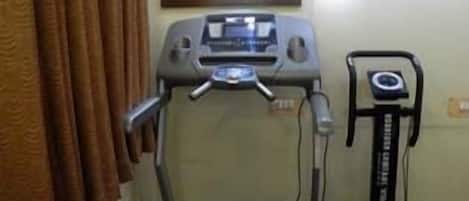 A room with a treadmill, a stationary bike, and a mirror on the wall.