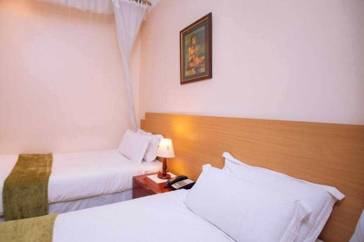 A hotel room with two beds, a bedside table with a lamp, a phone, and a picture on the wall.