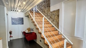 A modern interior with a wooden staircase, a stone wall, and a dining area with red chairs. - Hotel Punta Monpás (San Sebastián)