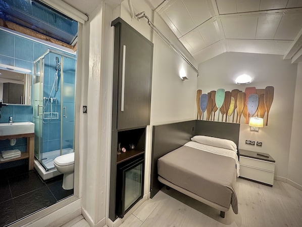 A bedroom with a bed, bedside tables, a wall-mounted lamp, a fireplace, and a shower area with a glass door. - Hotel Punta Monpás (San Sebastián)