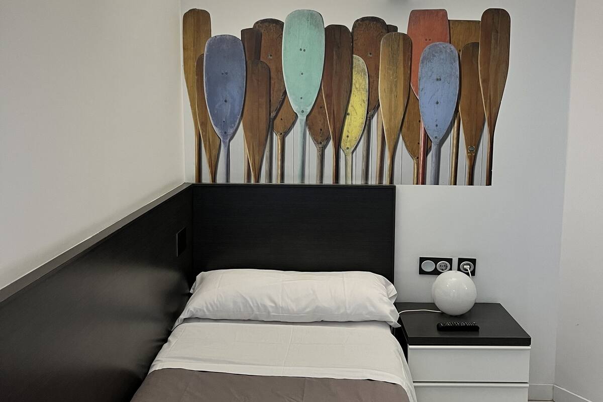 A modern bedroom with a bed, a nightstand with a lamp, and a wall-mounted shelf.