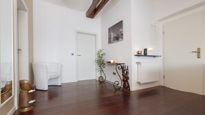 A hallway with a white door, a white chair, a plant, a small table with candles, and a radiator. - The Queen Luxury Apartments - Villa Giada (Hesperange)
