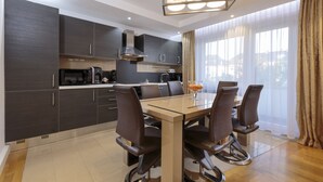 A modern kitchen with dark cabinetry, a central island, and a dining area with four chairs. - The Queen Luxury Apartments - Villa Giada (Hesperange)