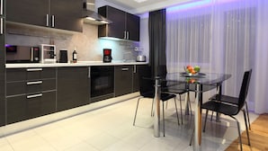 A modern kitchen with dark cabinets, a glass dining table, and a coffee maker. - The Queen Luxury Apartments - Villa Giada (Hesperange)