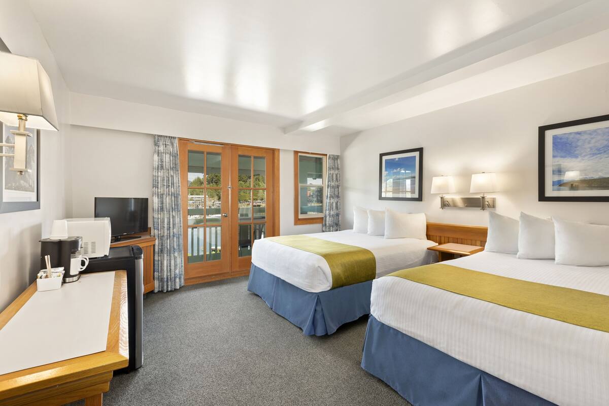 A hotel room with two beds, a desk, a television, and a balcony with curtains.