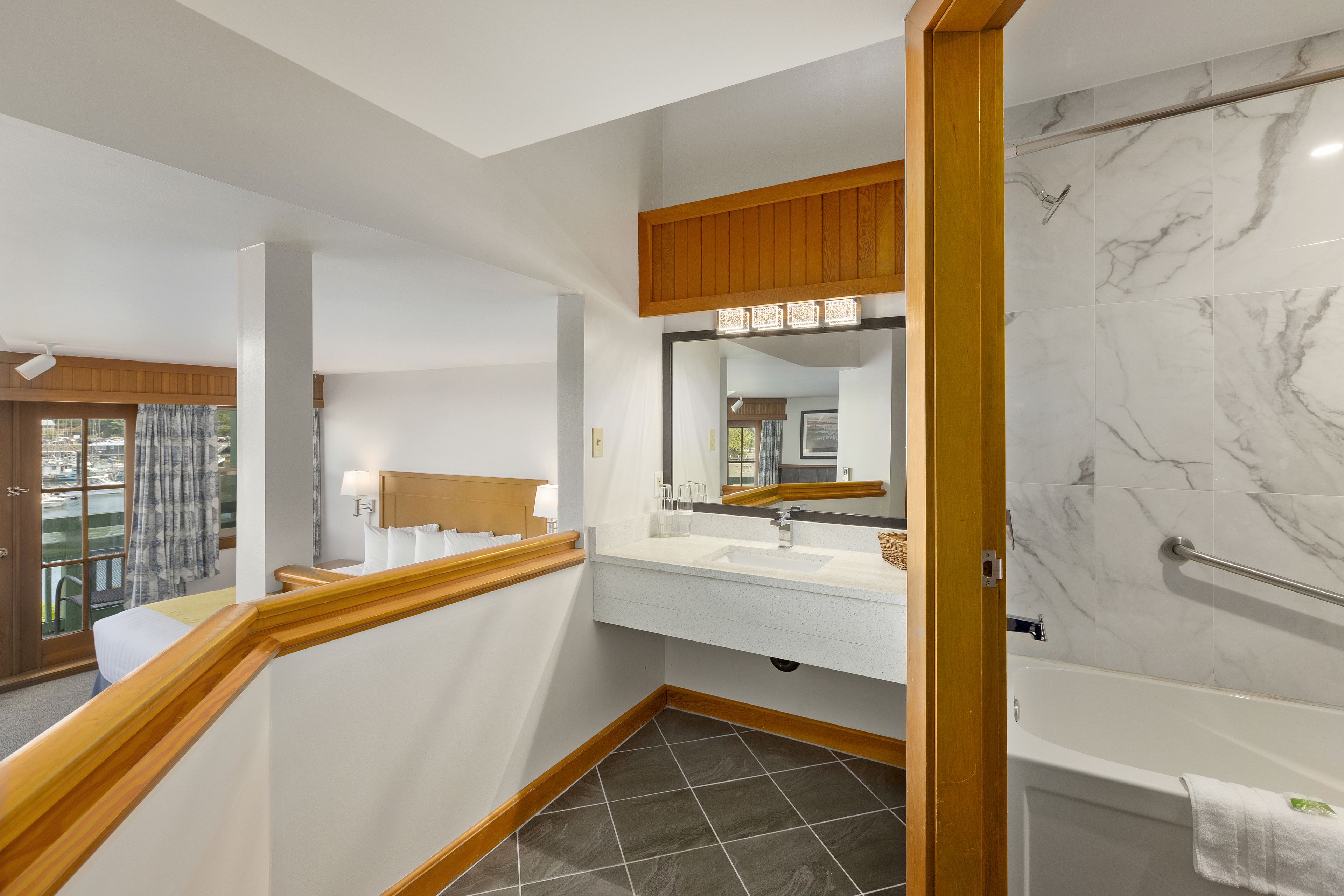 A modern bathroom with a marble shower, a wooden-framed vanity, and a large mirror.