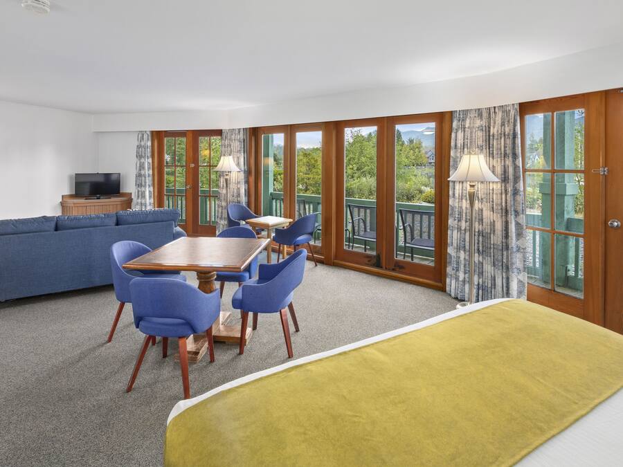 A room with a sofa, dining table, chairs, a TV, and large windows with a view of greenery and a body of water.
