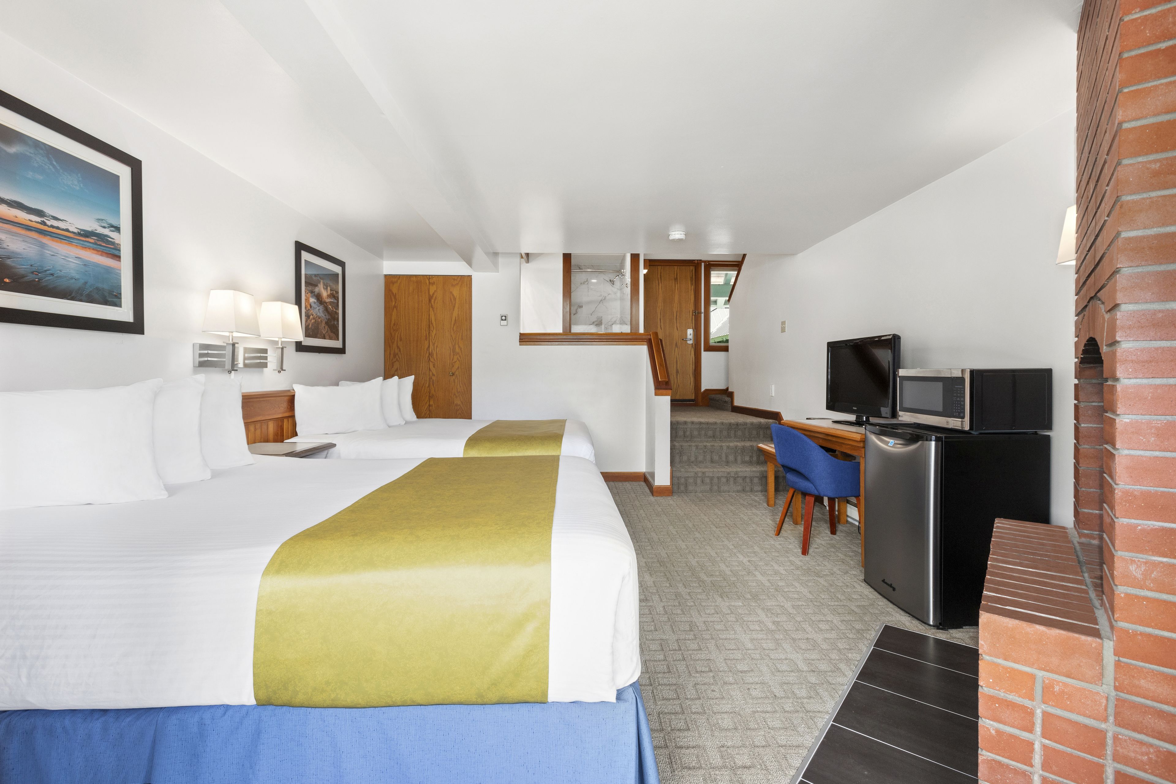 A hotel room with two beds, a desk with a computer, a television, and a brick fireplace.