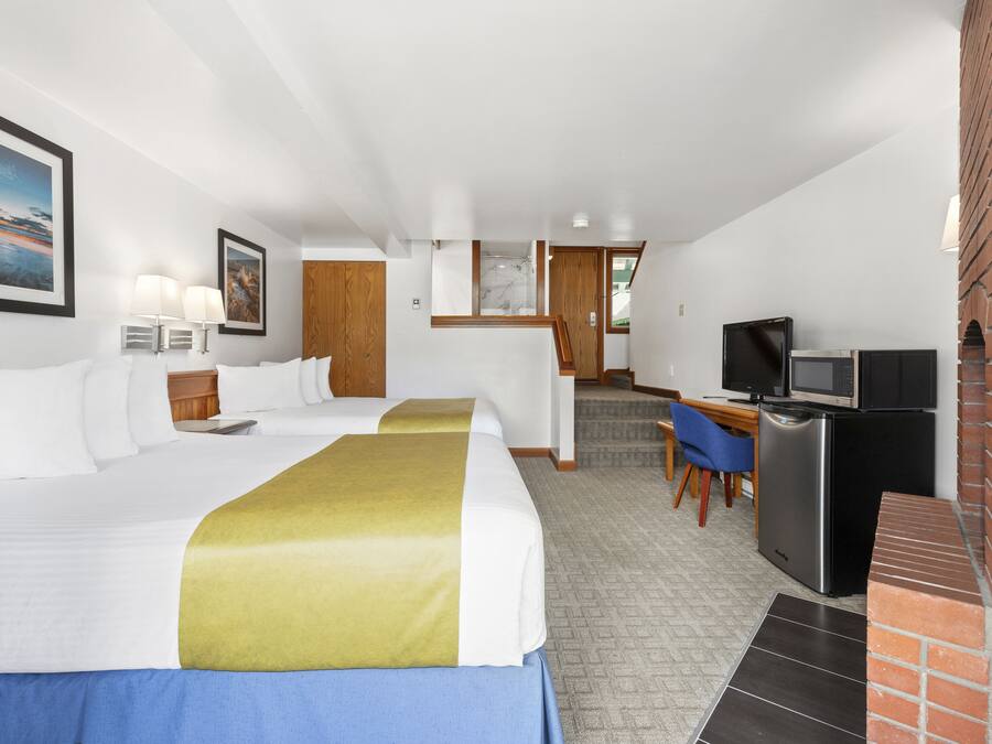 A hotel room with two beds, a desk with a computer, a television, and a brick fireplace.
