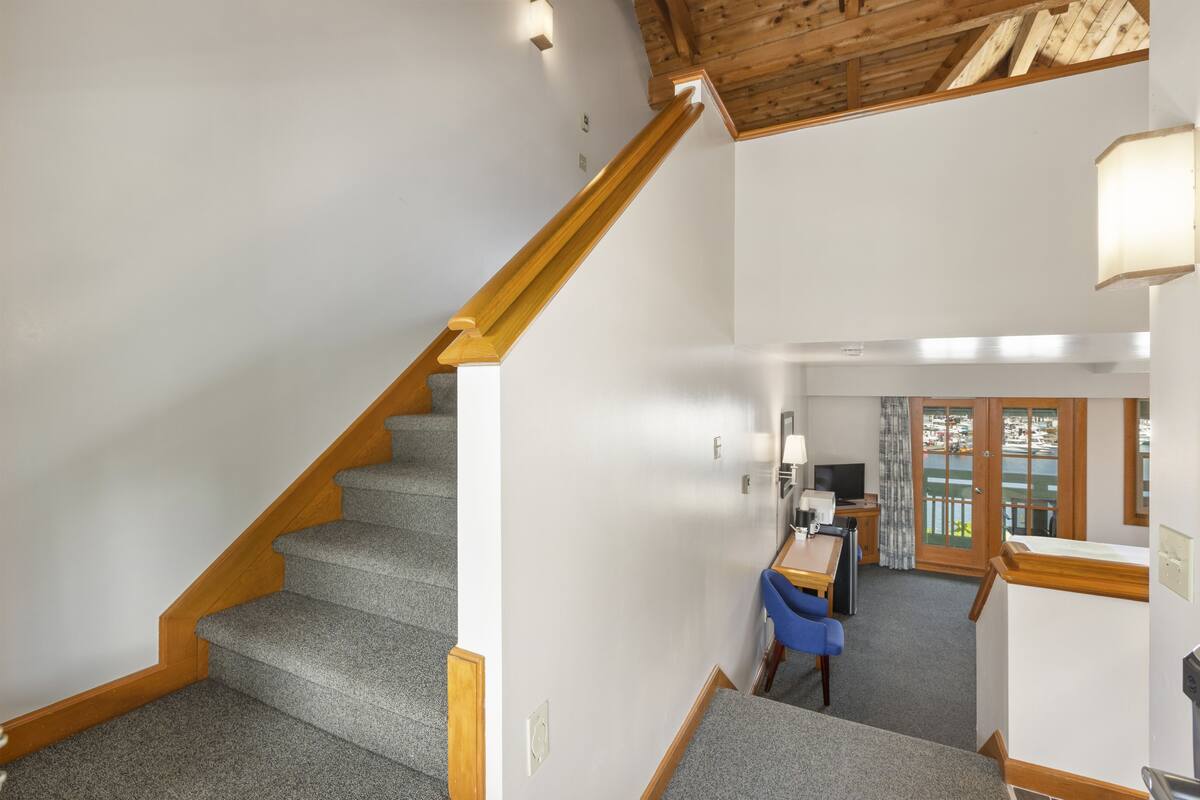 A staircase with wooden handrails leading to a room with a desk, chair, and a view of the outdoors.