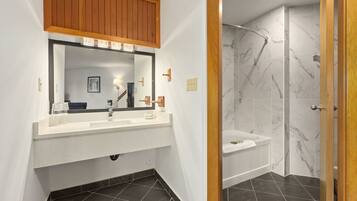 A bathroom with a white vanity, a mirror, a wooden cabinet, a bathtub, and a shower with marble tiles.
