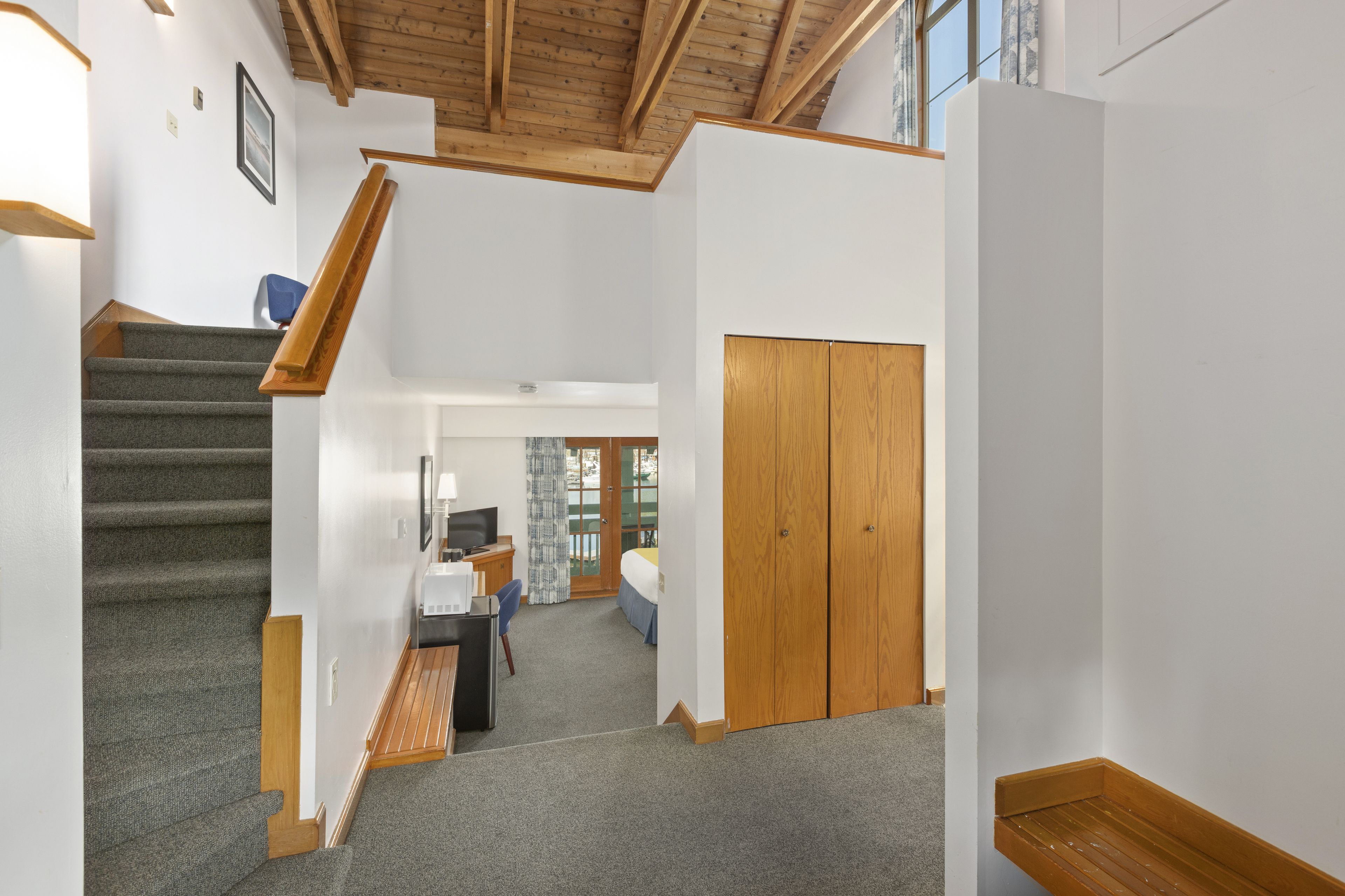 A hotel room with a staircase, a desk with a computer, a bed, and a wardrobe.
