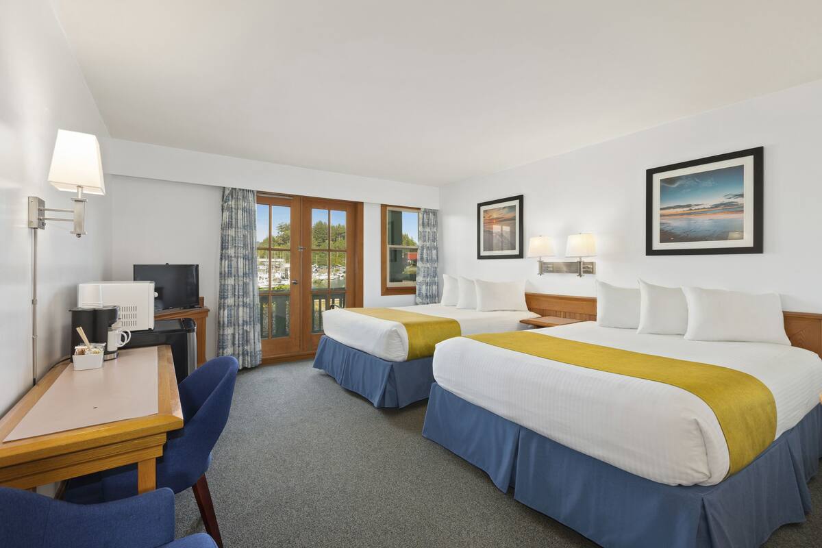 A hotel room with two beds, a desk, a chair, a TV, and a window with curtains.