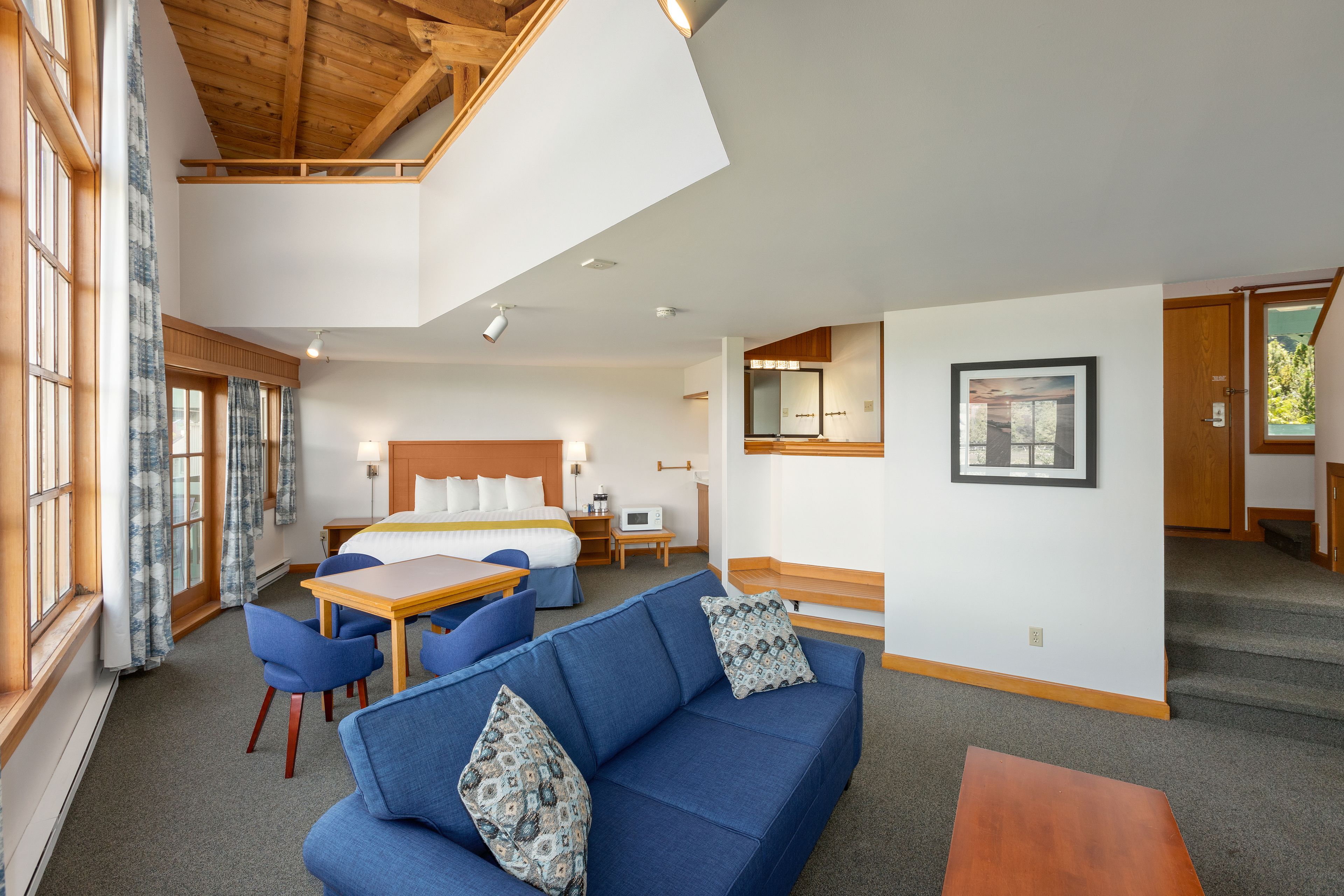 A hotel room with a lofted sleeping area, a dining table, blue sofa, and a staircase.