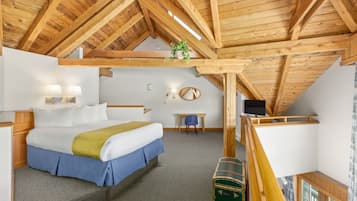 A bedroom with a wooden ceiling, a bed with white and blue bedding, a desk with a chair, and a green trunk.