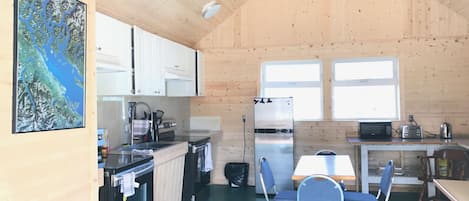 A wooden cabin interior with a kitchen, dining area, and a large window.
