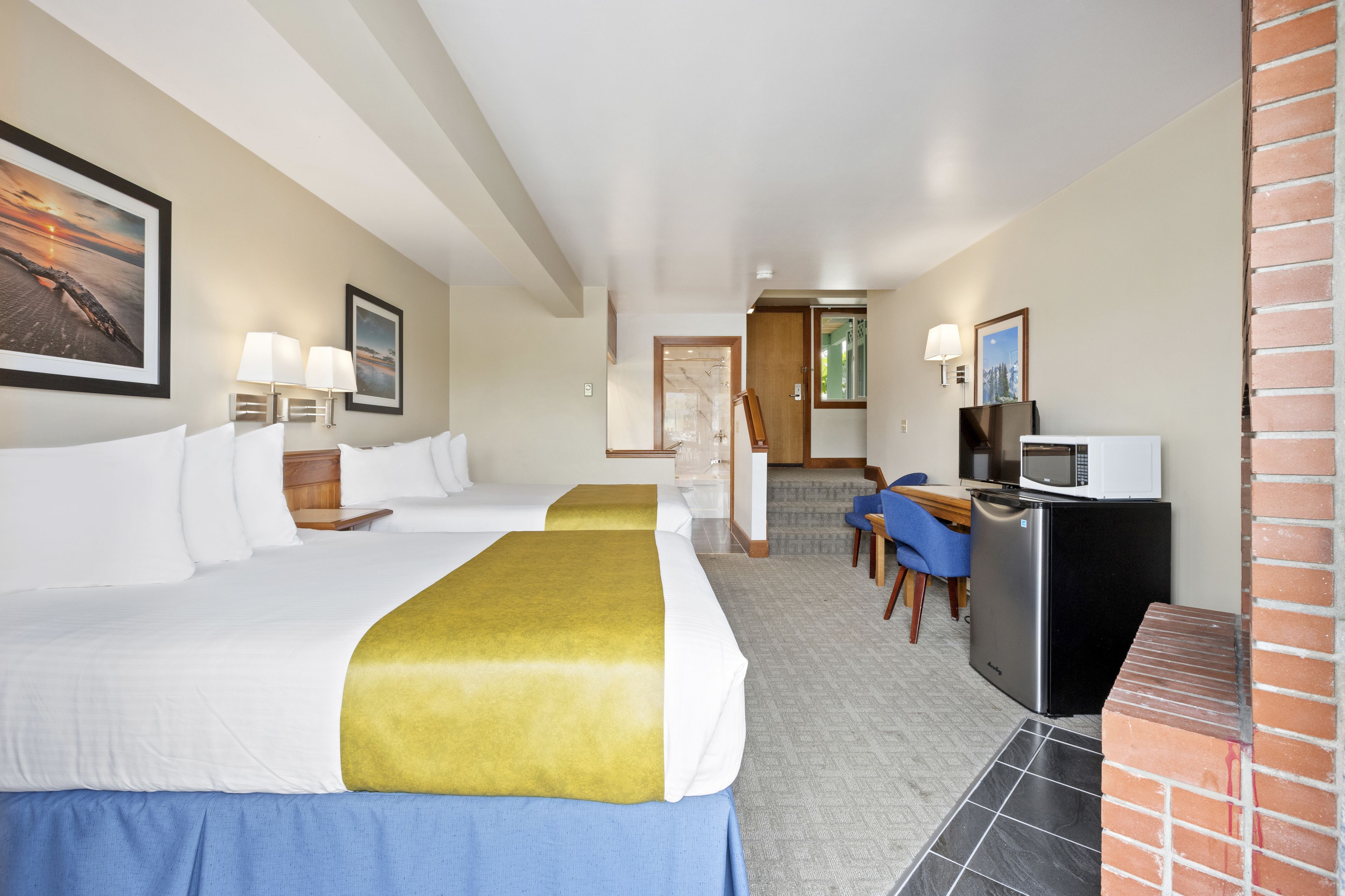 A hotel room with two beds, a desk, a microwave, and a TV.