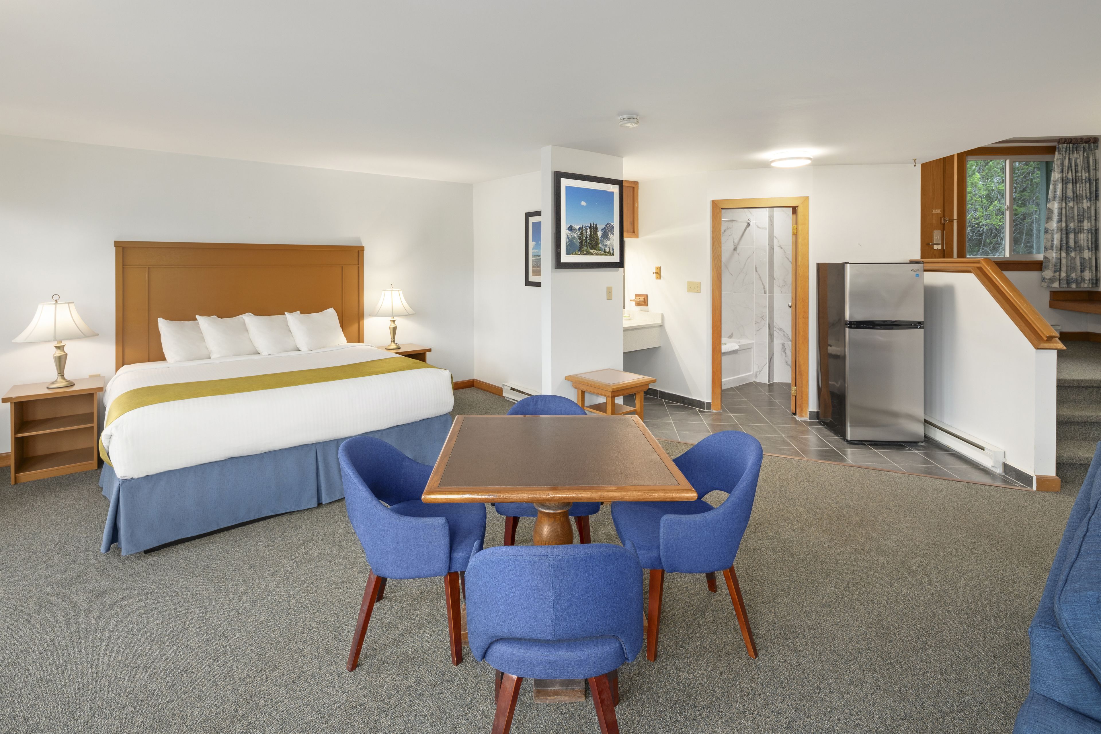 Hotelkamer met een bed, een tafel met stoelen, een koelkast, een kitchenette en een badkamer.