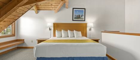 Une chambre avec un plafond en bois, un lit avec une literie blanche et bleue, deux lampes de chevet et un tableau encadré au mur.