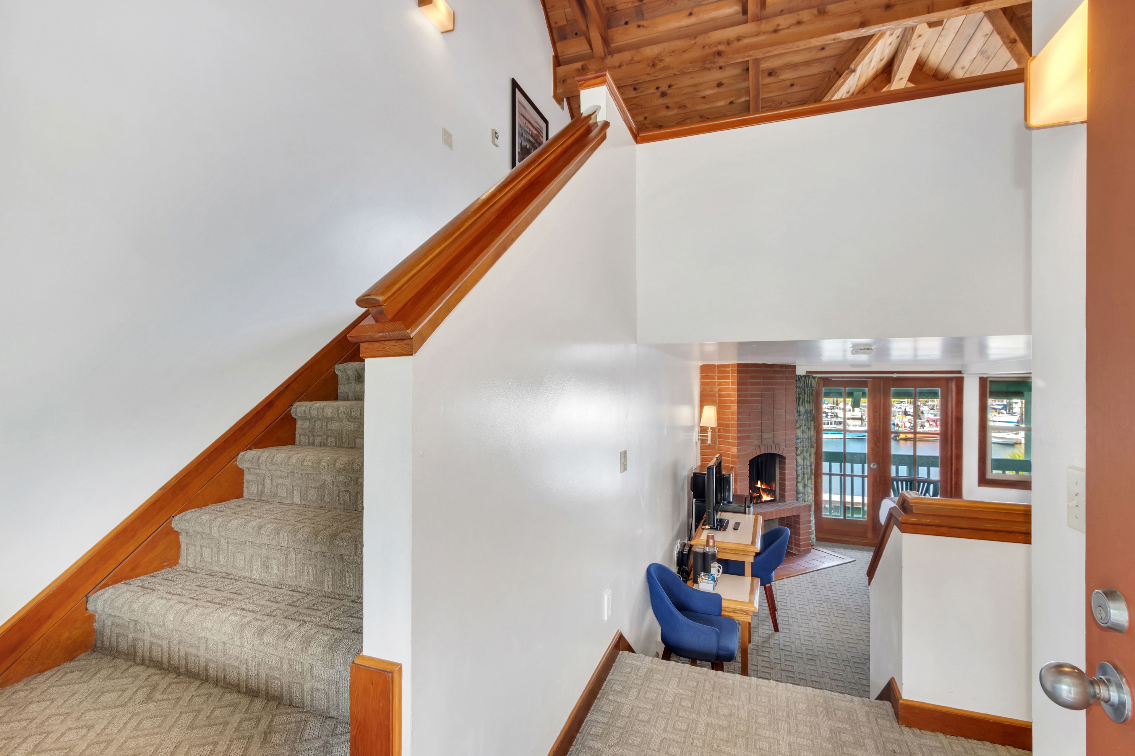 A staircase with carpeted steps leading to a living area with a fireplace, a dining table, and blue chairs.