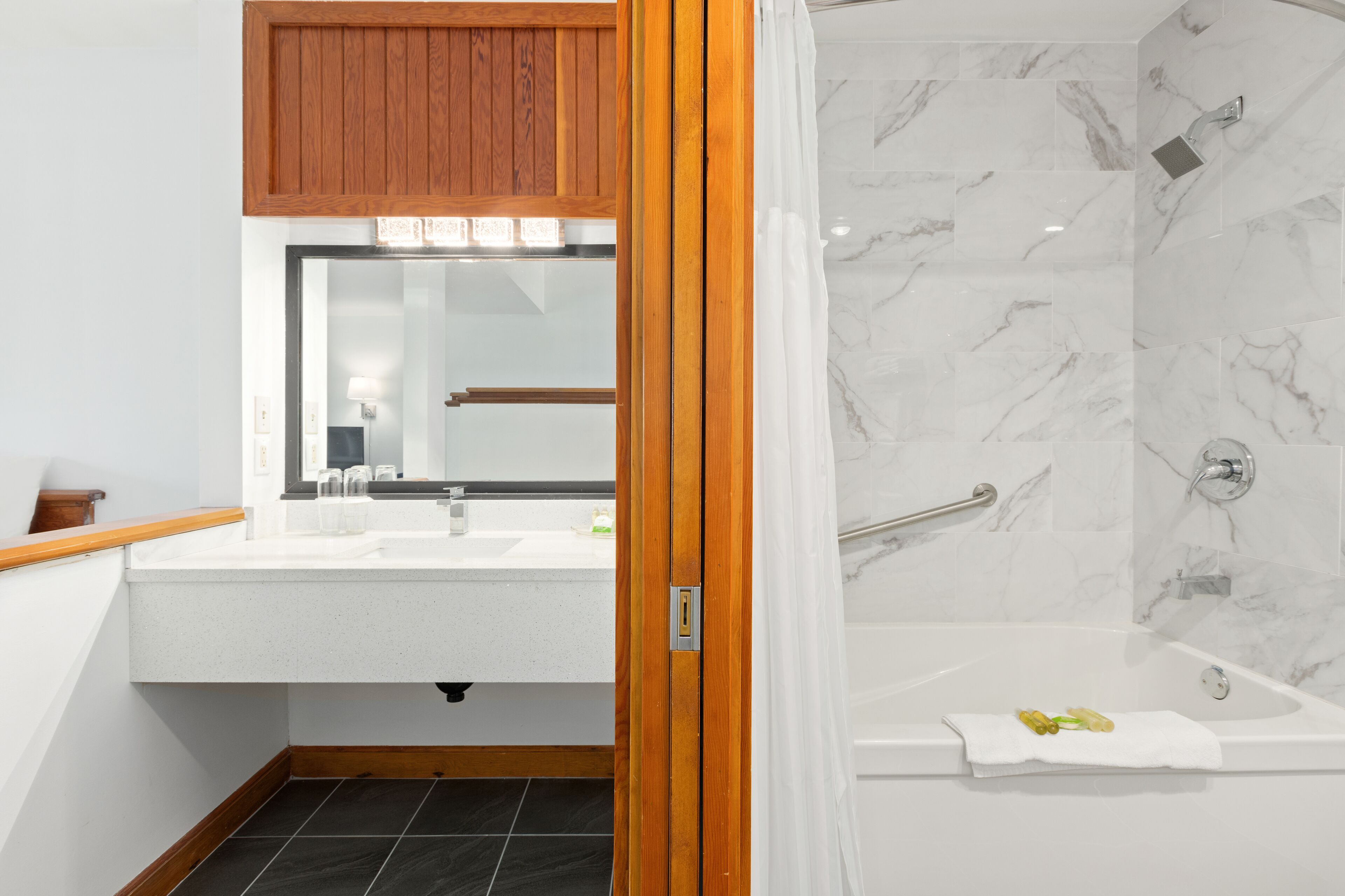 A modern bathroom with a wooden vanity, a large mirror, a shower with marble walls, and a bathtub.