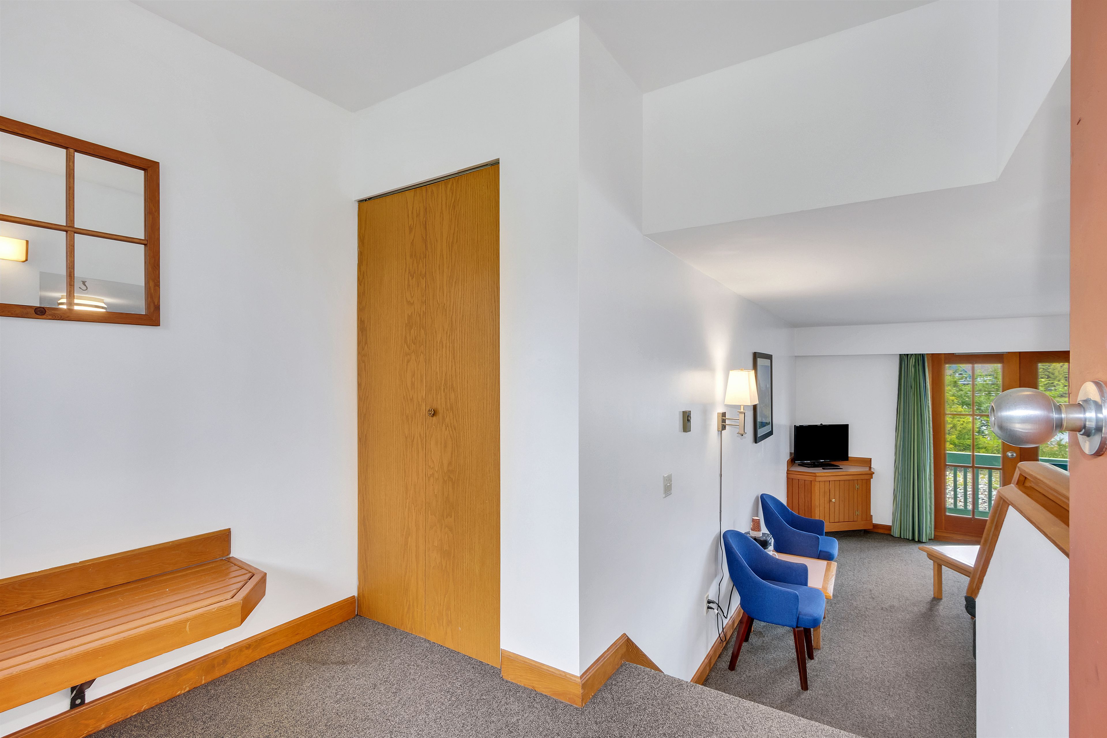 A hotel room with a wooden bench, a TV, and a desk with chairs.