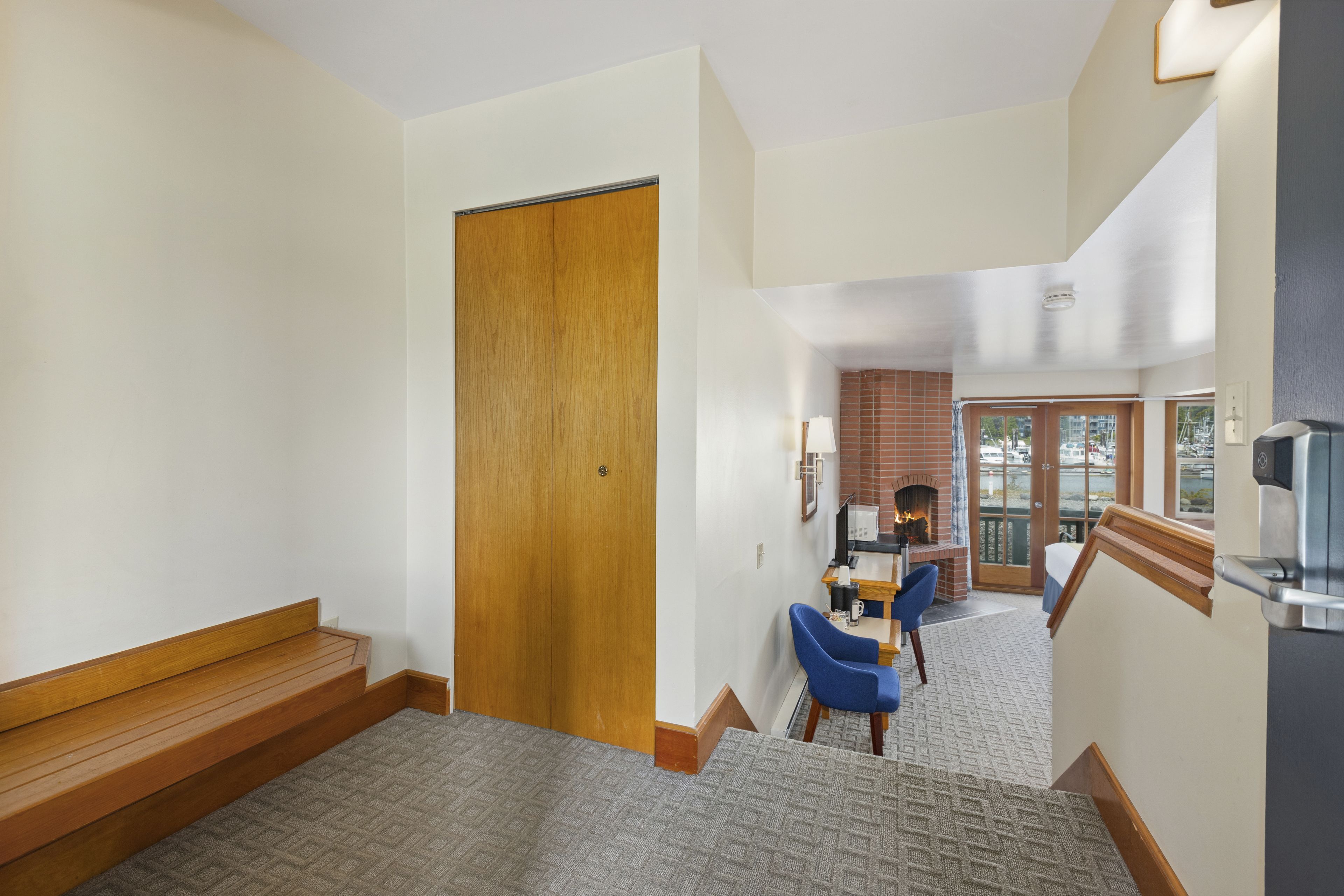A hotel lobby with a wooden door, a blue chair, a fireplace, and a view of the outside.