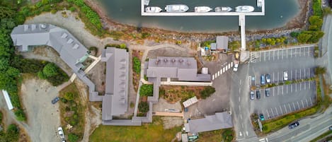 An aerial view of a coastal property with a marina, parking lot, and buildings with multiple roofs.