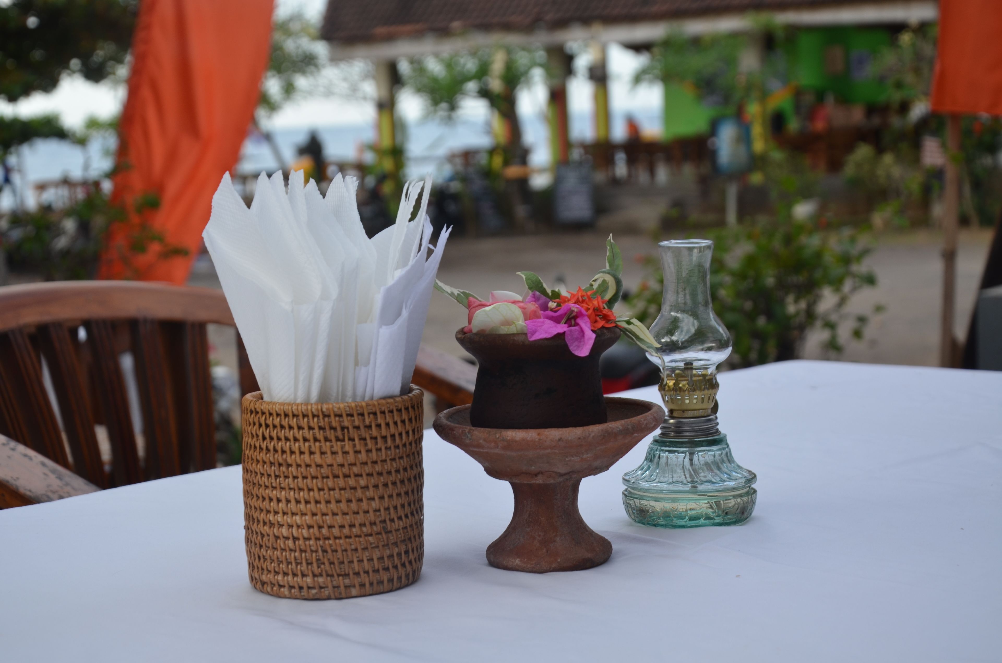 A table with a woven basket holding napkins, a clay pot with flowers, and a glass bottle.