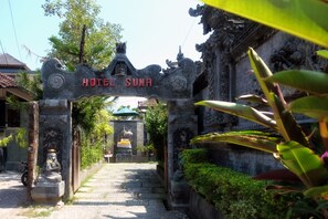 Um arco de pedra com a inscrição "HOTEL SUMA" dando acesso a um caminho.
