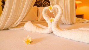 Uma cama com lençóis brancos e duas toalhas dobradas em formato de cisnes, com flores.