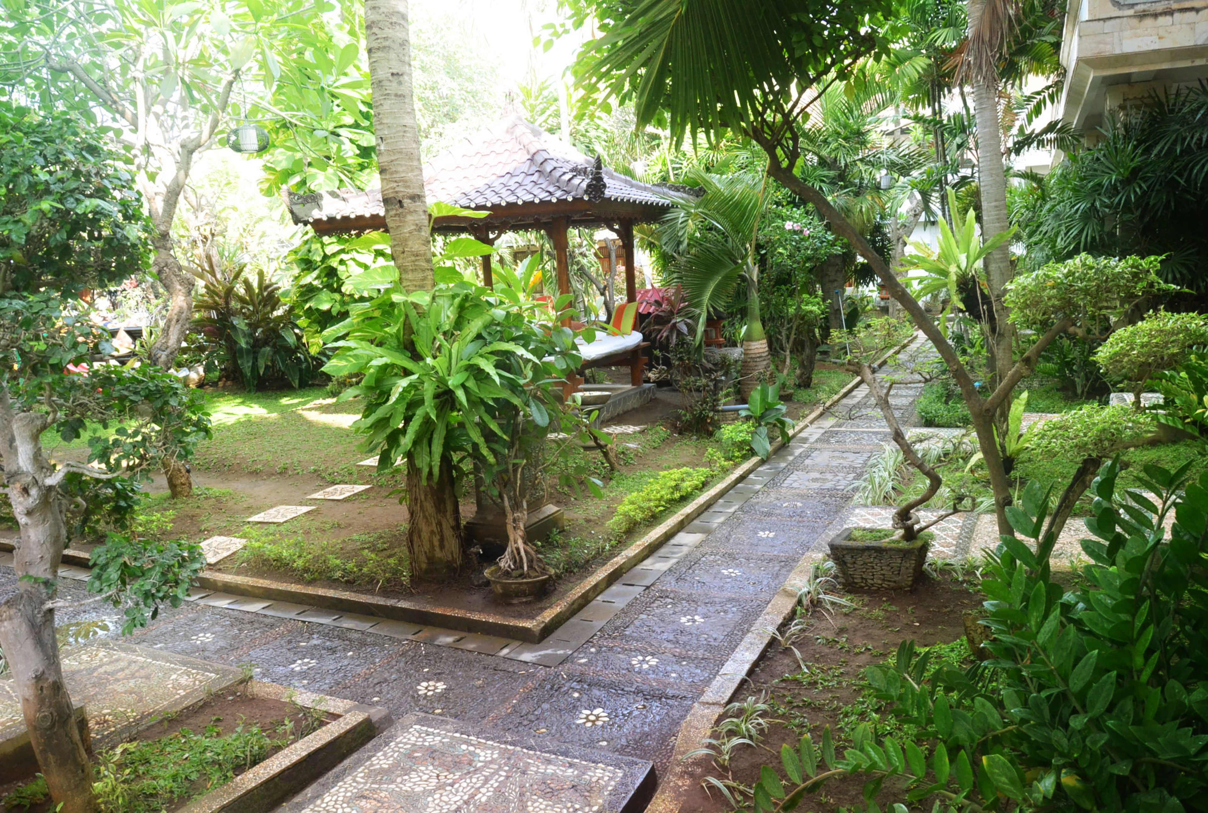 A garden with a gazebo, a stone pathway, and various tropical plants.