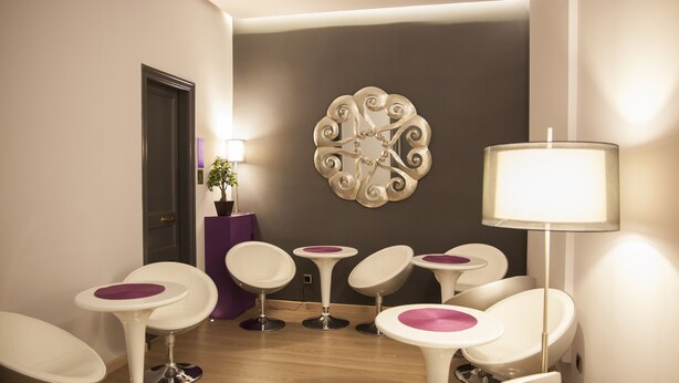 Un área de espera moderna con sillas blancas, un muro de acento púrpura y una pieza decorativa en la pared.