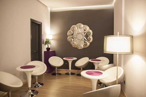 Un área de espera moderna con sillas blancas, un muro de acento púrpura y una pieza decorativa en la pared.