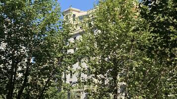 Un edificio de varios pisos con estilo arquitectónico clásico, rodeado de árboles y un cielo azul despejado.