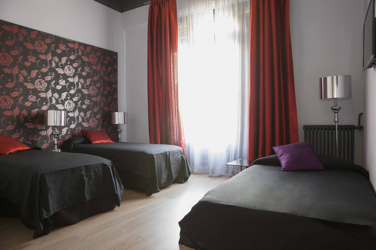 Et hotelværelse med to senge, en radiator, en lampe og et vindue med gardiner.