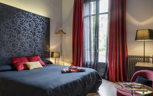 A modern hotel room with a large bed, red curtains, a patterned wall, and a side table with a lamp. - Umma Barcelona Bed & Breakfast Boutique (Barcelona)