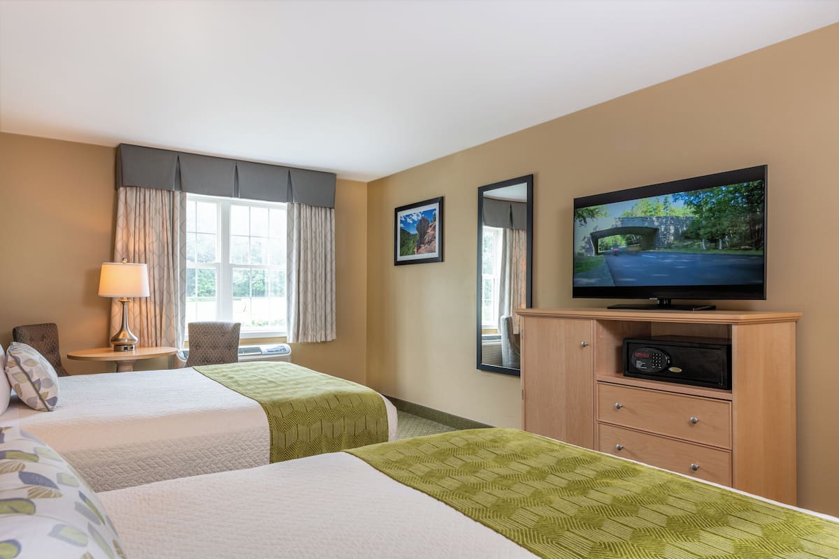 A hotel room with two beds, a television, a desk with a lamp, and a view of a bridge.