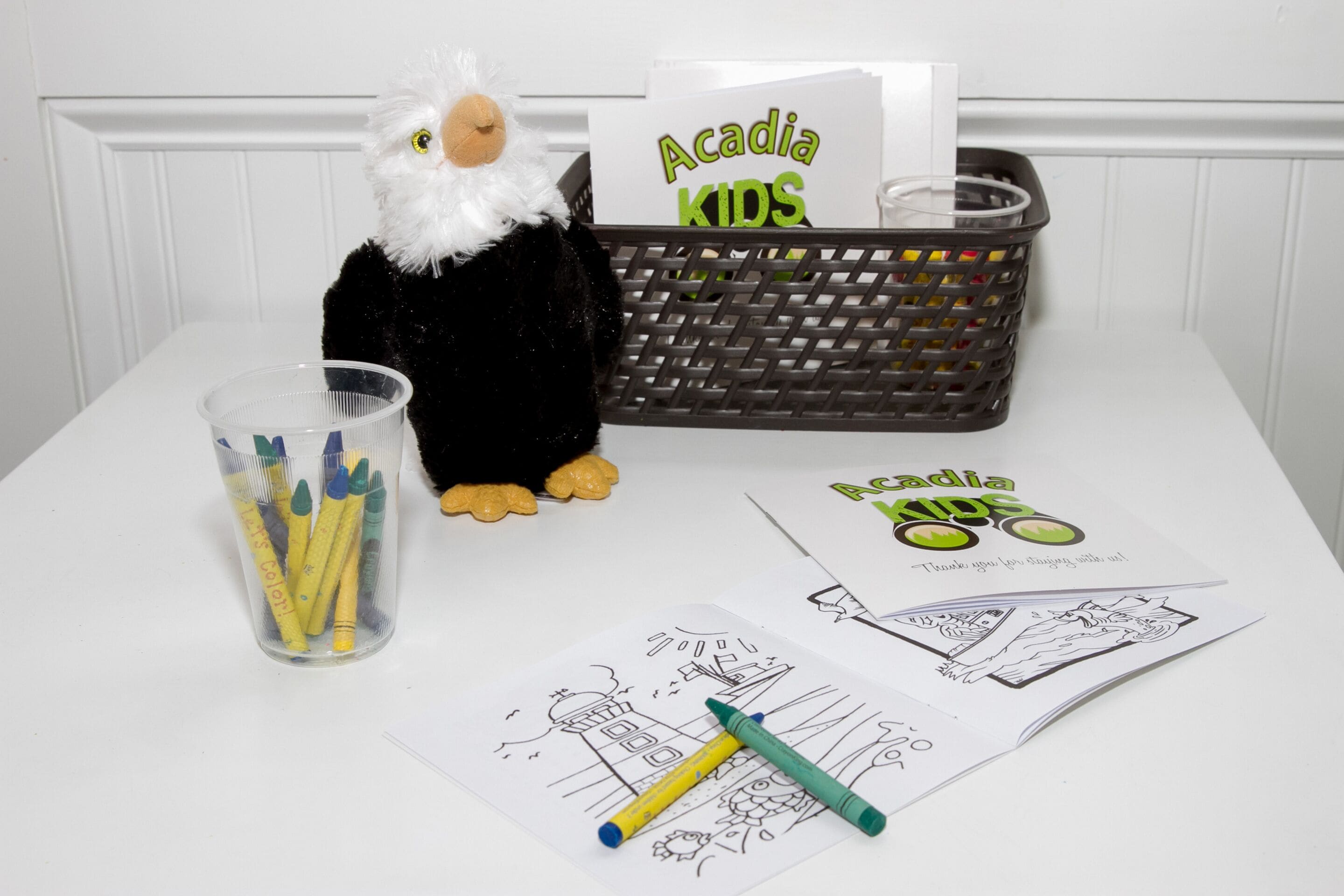 A table with a stuffed animal, a basket with a sign, and some coloring materials.
