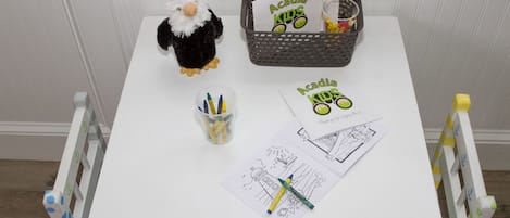Una mesa pequeña con un peluche, una cesta con cartas, una taza con rotuladores y un par de hojas para colorear.