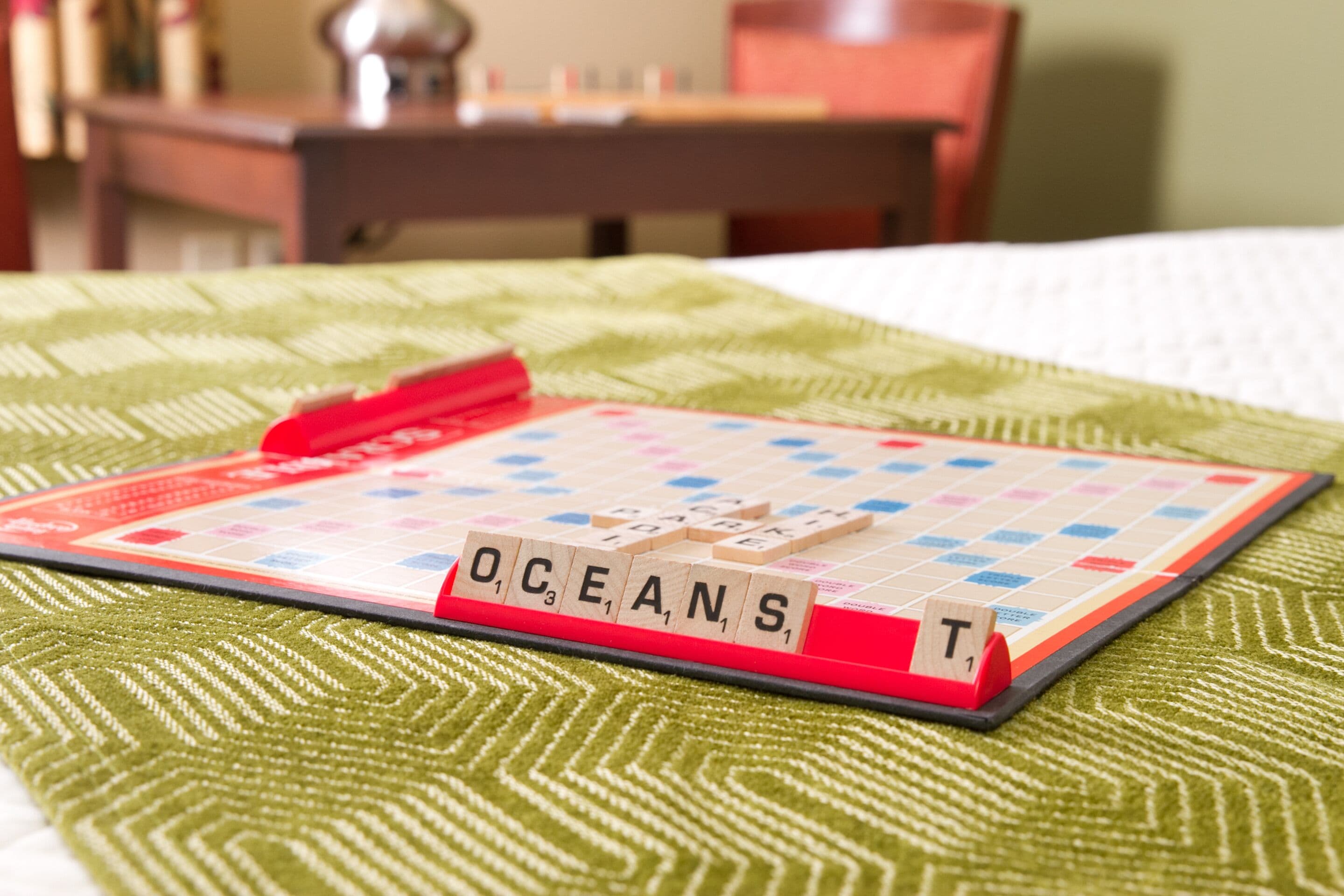 A Scrabble game on a bed with a green patterned bedspread.