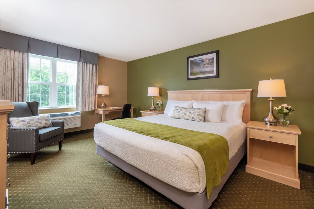 A hotel room with a large bed, a desk, a chair, and a window with curtains.