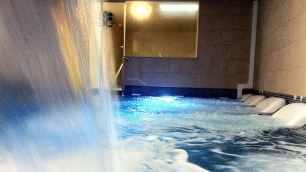 Ein Whirlpool mit Wasserdüsen, ein Duschbereich und eine geflieste Wand.