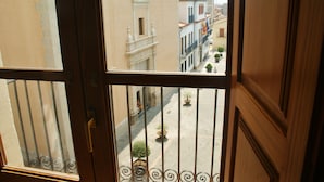 Blick aus einem Fenster mit Metallgeländer auf eine Straße mit Gebäuden und Pflanzgefäßen.