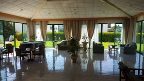A spacious indoor area with a pool table, comfortable seating, and large windows offering a view of a well-maintained garden. - Mandalena Hotel Apts (Paralimni)
