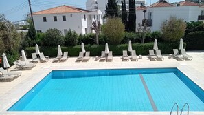 A rectangular swimming pool with tiled edges and a clear blue center, surrounded by lounge chairs and umbrellas. - Mandalena Hotel Apts (Paralimni)